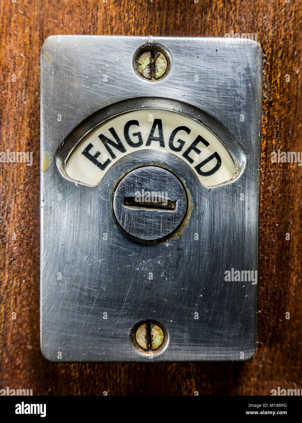 Tradizionale metallo vecchio "impegnato" segno / avviso avvitato ad un blocco porta di legno, per mostrare agli altri utenti che un armadio wc è occupato. Inghilterra, Regno Unito. Foto Stock