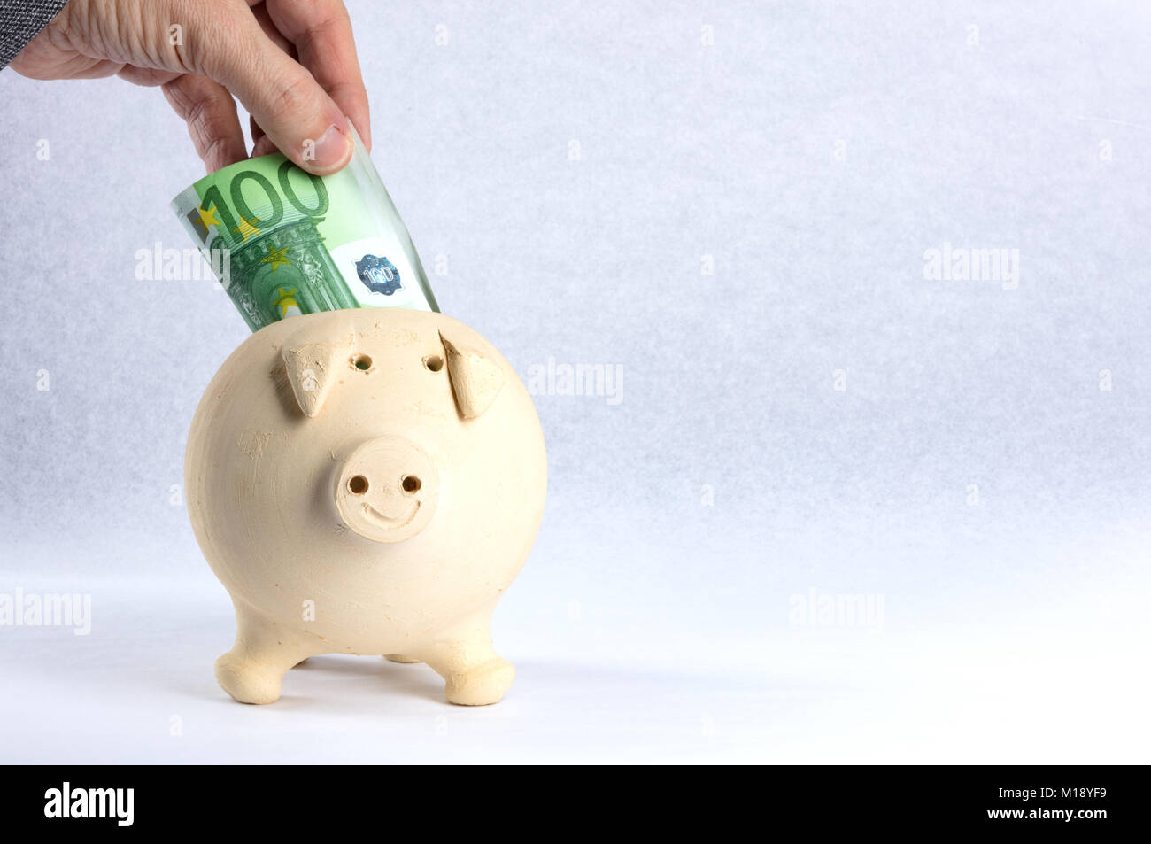 Una mano messa all'interno del salvadanaio di risparmio, di colore giallo, 100 euro su un libro bianco sullo sfondo. Spazio libero per il testo Foto Stock