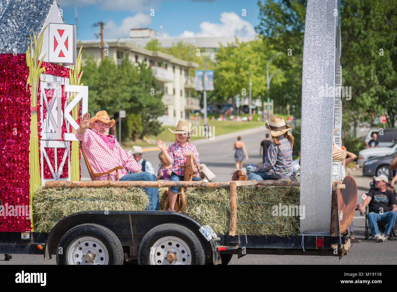 Persone in abito occidentale onda per la folla dalla loro azienda parata a tema galleggiante a Stampede annuale parata nel centro di Williams Lake, BC, Canada. Foto Stock
