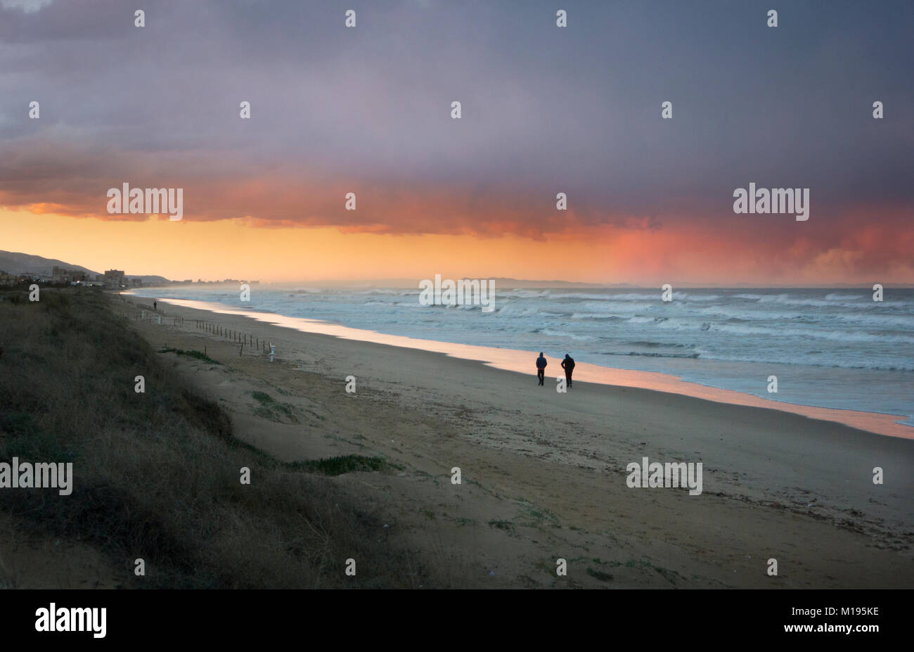 Due persone che camminano sulla spiaggia al tramonto su una serata di tempesta Foto Stock