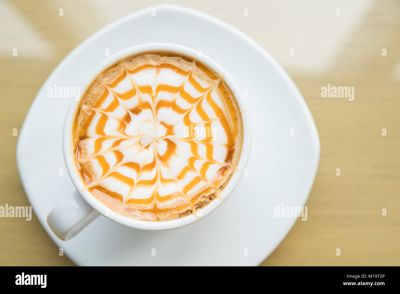 A caldo il caffè macchiato con caramello in tazza bianca sulla tavola di legno dalla luce della finestra, Tabella vista superiore Foto Stock