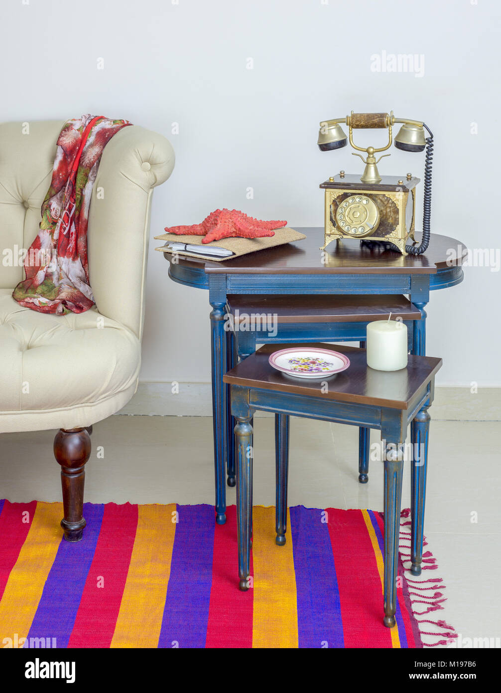 Interior shot di vecchi golden apparecchio telefonico, bianco candela, stelle marine rosse e colorati ornano la piastra al di sopra di tre tabelle nidificate con gambe blu Foto Stock