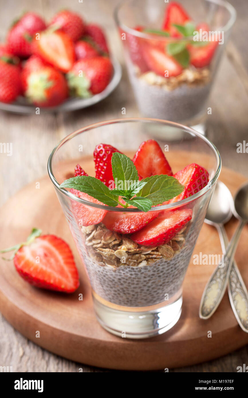 La dieta sana prima colazione. budino di Chia, fragole e muesli in un bicchiere , di fragole fresche sul vecchio sfondo di legno Foto Stock