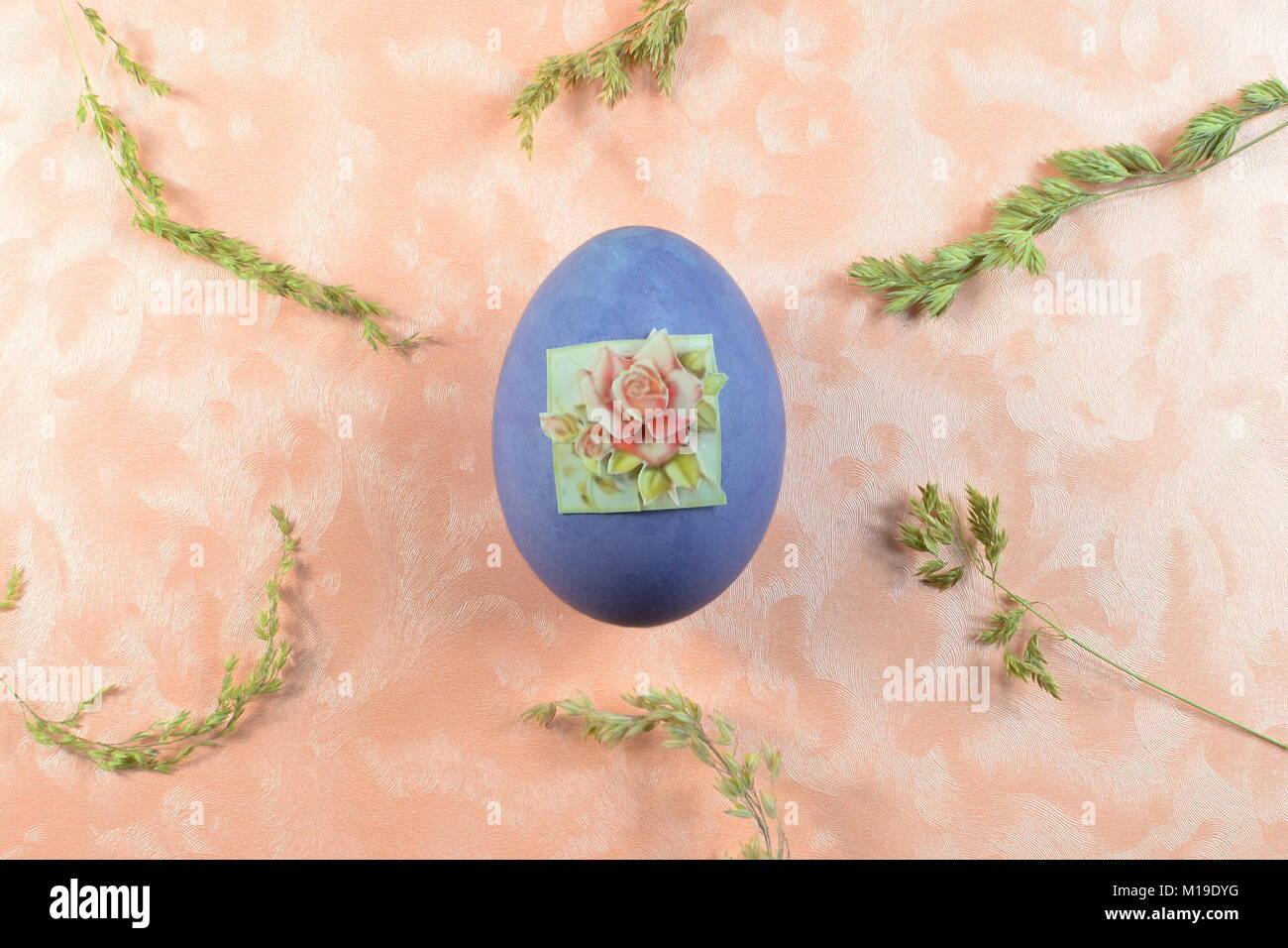 Un singolo uovo viola giace su una rosa di sfondo con erba e fieno Foto Stock