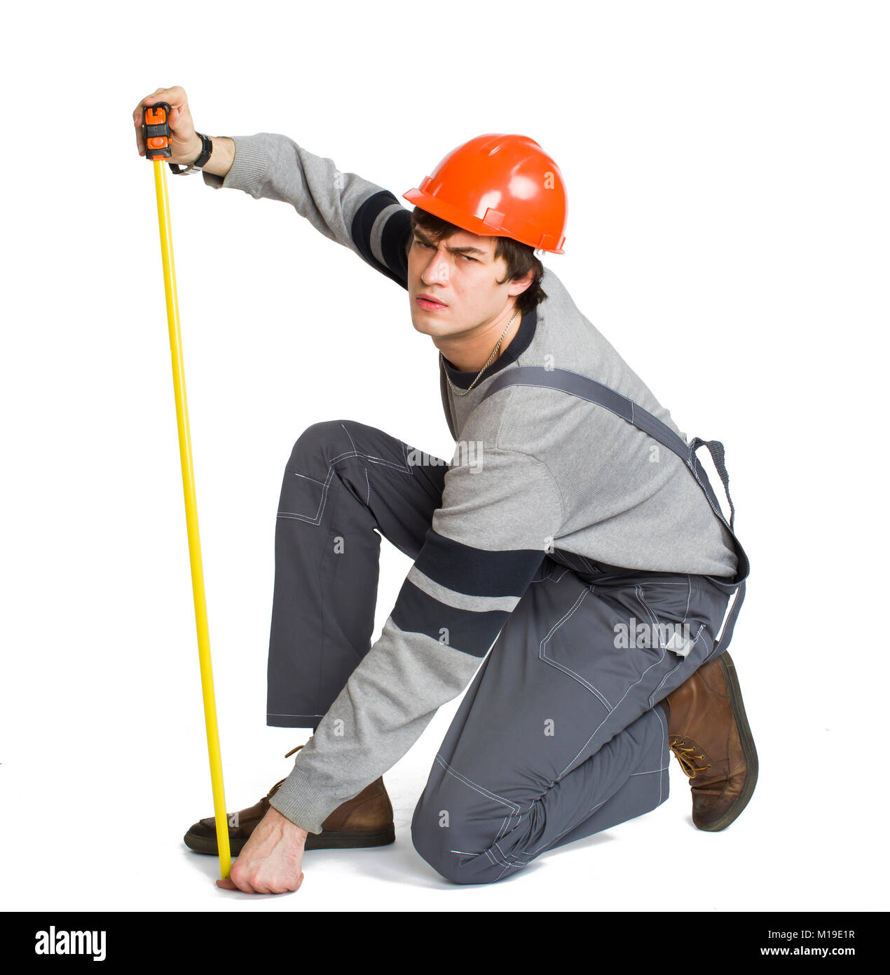 Un giovane uomo nel lavoro abiti di colore grigio e arancione casco duro la misura della zona di metrica in camera. Foto Stock