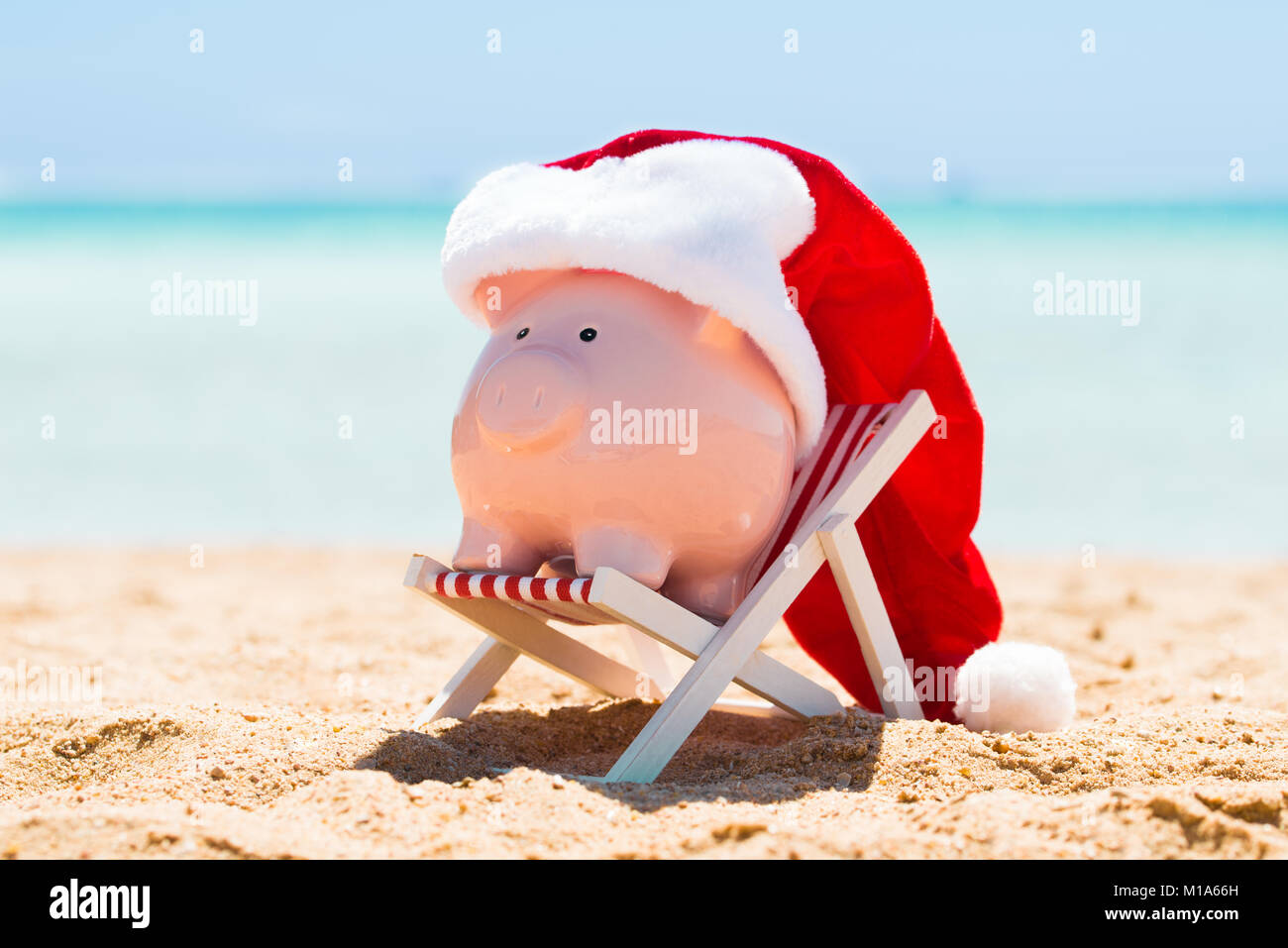 Una rosa Salvadanaio con Santa Hat mantenuta sulla sedia a sdraio in spiaggia Foto Stock