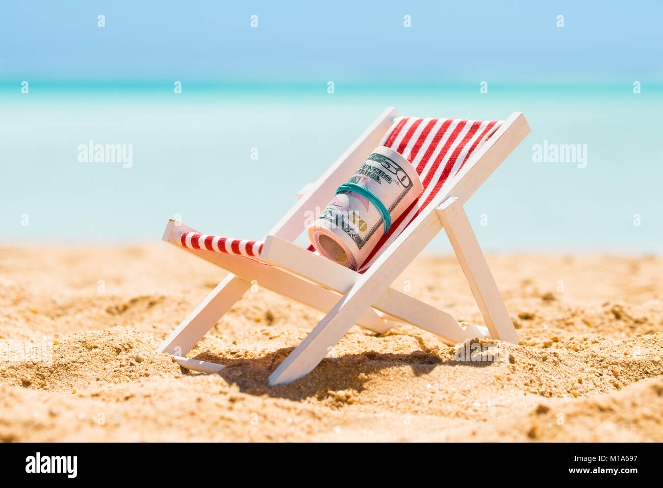 Arrotolato a fascio di cinquanta dollari banconote in miniatura sulla sedia a sdraio in spiaggia Foto Stock