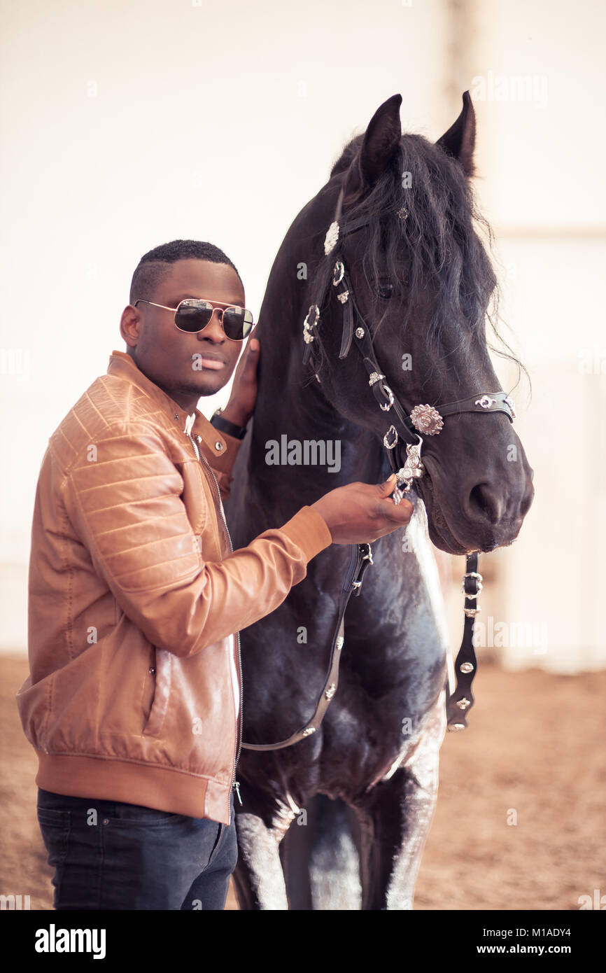 L'uomo africano indossando occhiali da sole vicino a cavallo nero in hangar  Foto stock - Alamy