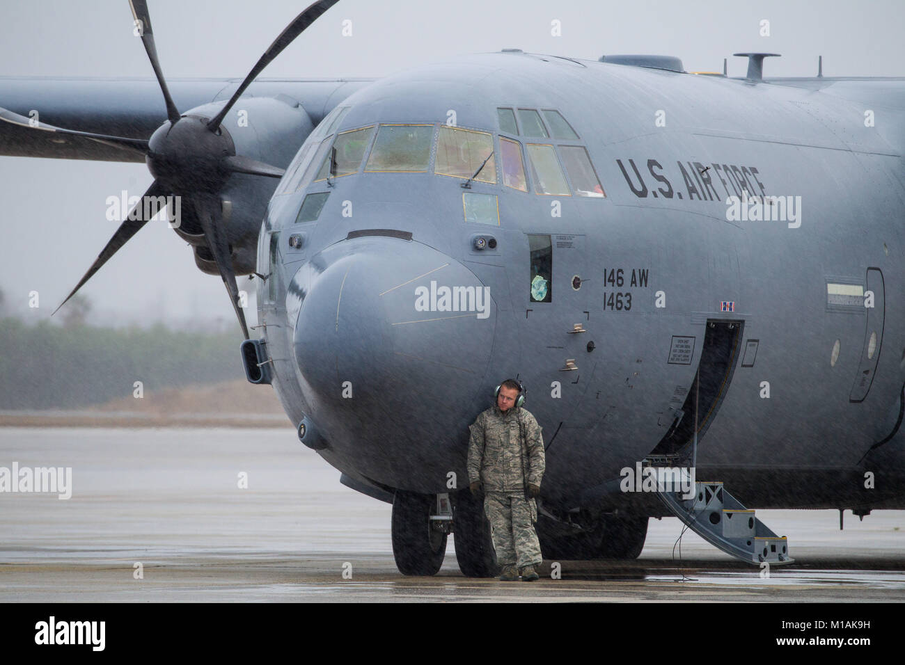 Un aviatore da 146Airlift Wing, California Air National Guard, utilizza il naso di un C-130 di schermatura stesso dalla pioggia su asfalto a forze congiunte Training Base, Los Alamitos, Gen 9, 2018. Il velivolo ha portato il direttore della Air National Guard e il suo staff per la base durante un tour della California la Guardia Nazionale di unità e impianti. (Air National Guard foto di Senior Airman Crystal Housman) Foto Stock