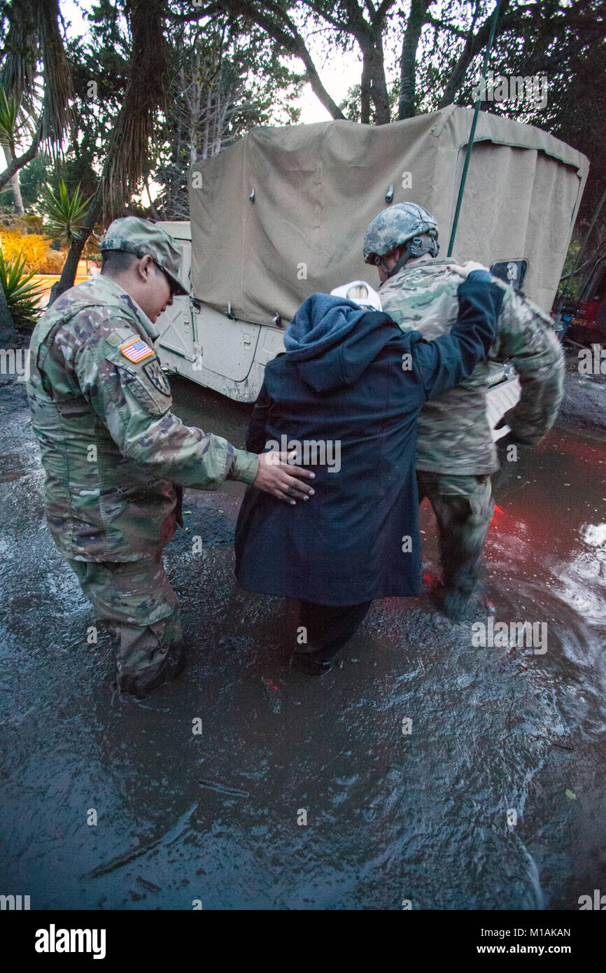 Sgt. Jose Paiz, destra e Staff Sgt. Michael Aguilar, a sinistra, entrambi del composito 1114th Truck Company, California Guardia nazionale, guida una donna attraverso dense knee-fango profondo Gen 12, 2018 da un Montecito, California, la Casa del Soldato' Humvee. Il 1114th è accreditato con il salvataggio o evacuazione di più di 1.800 persone nella zona Montecito a seguito di una frana di fango mortale che ha colpito la città nel predawn ore gen. 9. (Air National Guard foto di Senior Airman Crystal Housman) Foto Stock