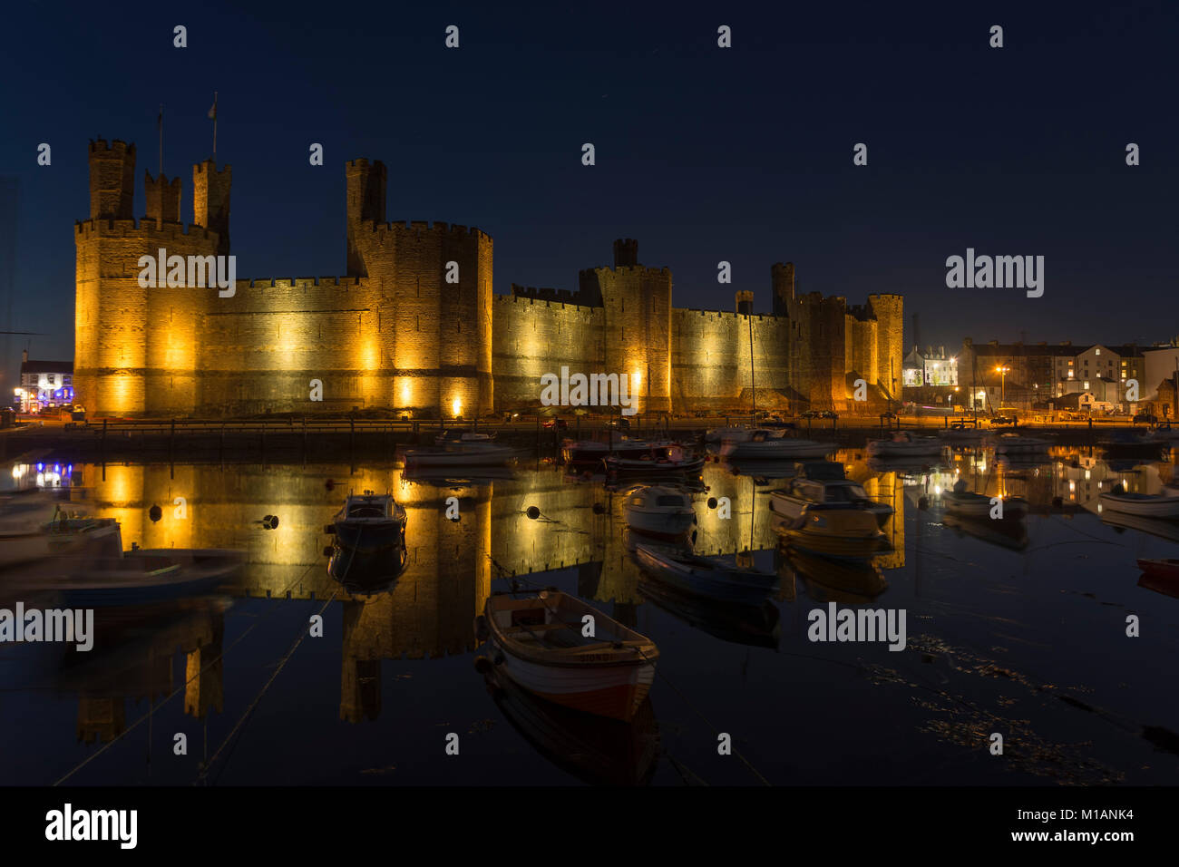 Caernarfon Castle e il porto con barche e riflessi di notte, costa del Galles Settentrionale Foto Stock