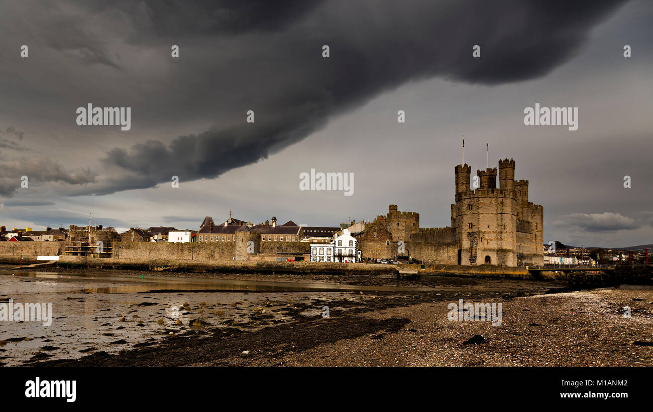 Il castello e la città a Caernarfon sulla costa settentrionale del Galles sotto pesante cloud Foto Stock