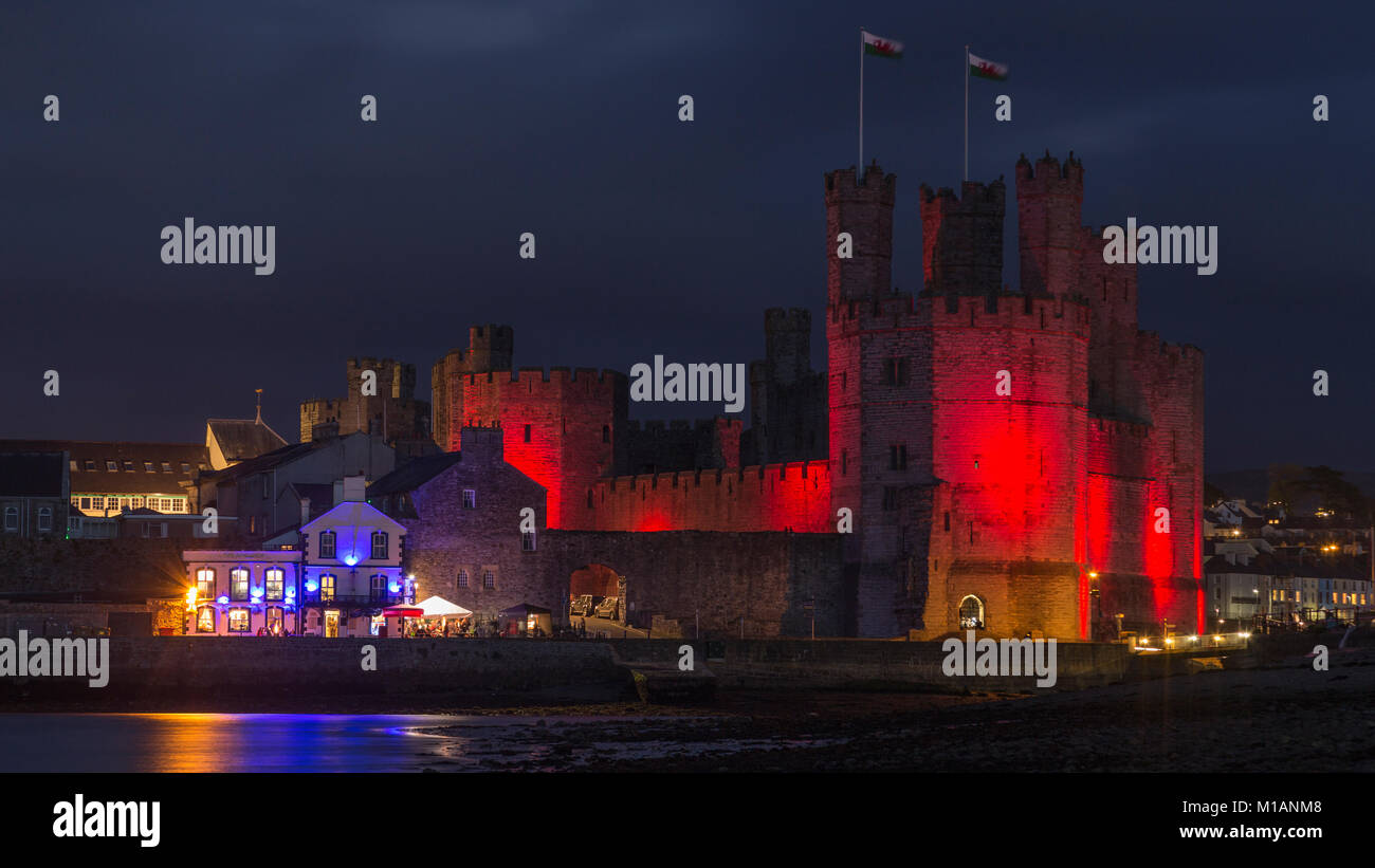 Caernarfon Castle di notte con illuminazione rossa per il giorno del ricordo, costa del Galles Settentrionale Foto Stock