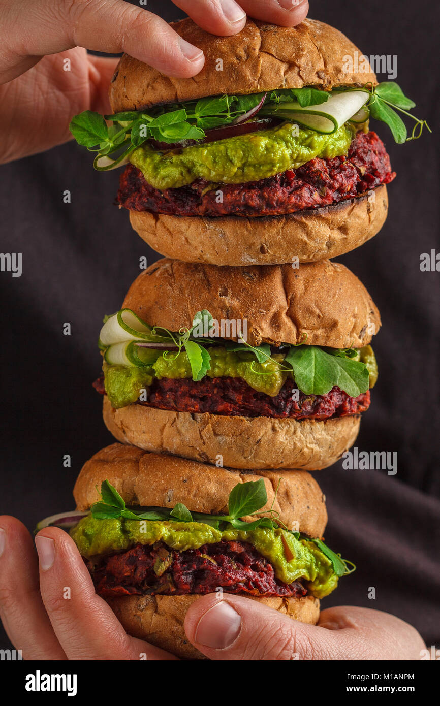 Vegano hamburger sani nelle mani dell'uomo. Vegan barbabietole hamburger di ceci con verdure, guacamole e segala ciambelle. Sano cibo vegan concetto. Foto Stock