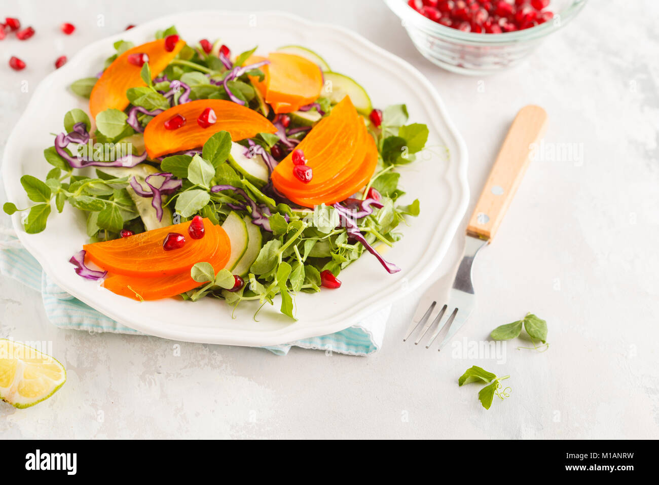 Persimmon insalata con foglie di piselli e melograno. Una sana alimentazione vegetariana concetto. Foto Stock