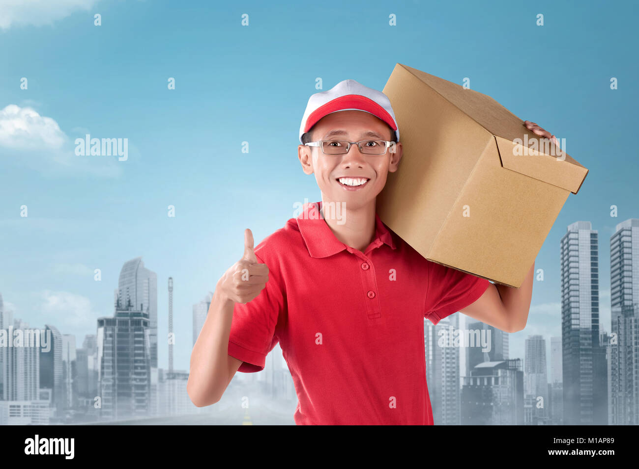 Felice corriere asiatico uomo che porta una scatola di cartone sulla spalla con il paesaggio sullo sfondo Foto Stock