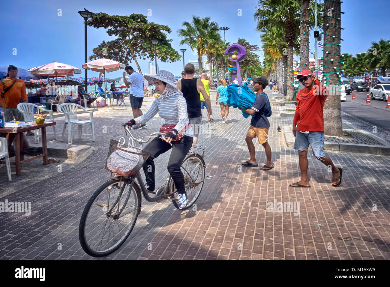 Thailandia scena di strada con la donna in sella ad una bicicletta sul marciapiede e persone di andare circa la loro routine quotidiana. Pattaya beach road, sud-est asiatico Foto Stock