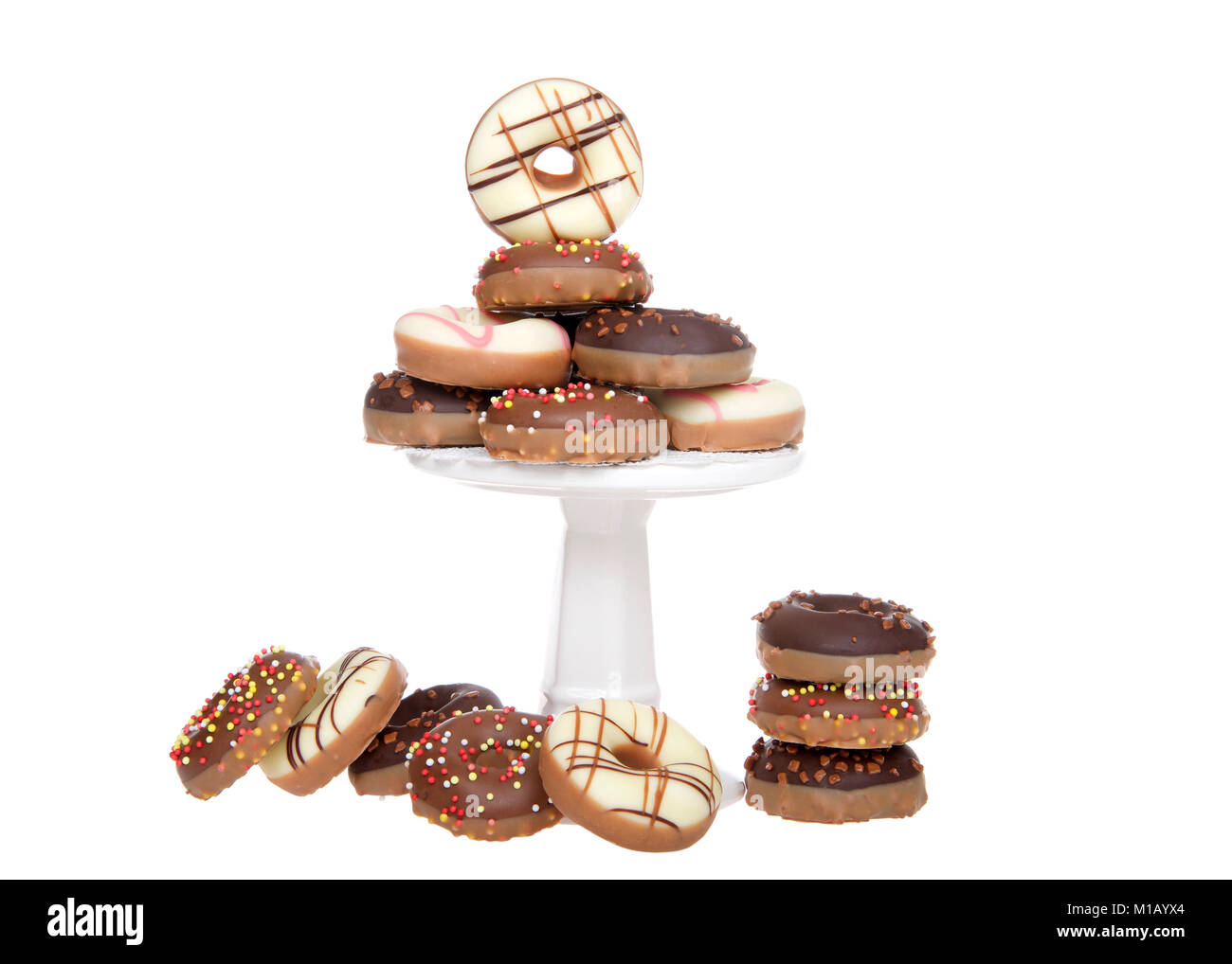 Molte piccole ciambelle rivestite di Candy e decorate con un pizzico impilati su un piccolo piedistallo con extra sul tavolo, isolato su bianco. Foto Stock