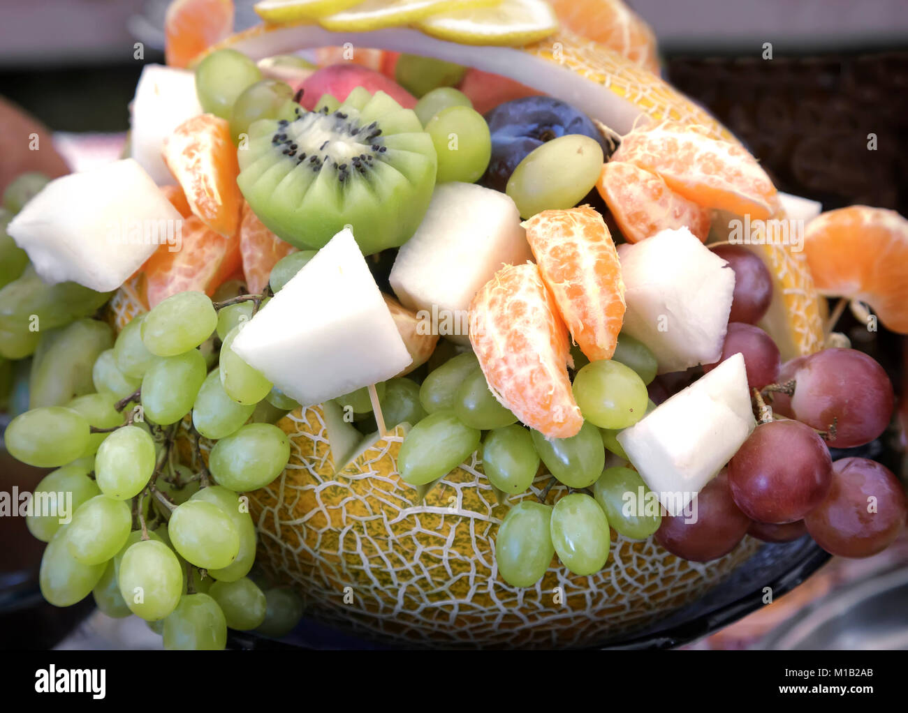 Grande zucca, decorato nella forma di un cestino e riempito con una varietà di frutta: uva, kiwi, banane, tangerini Foto Stock