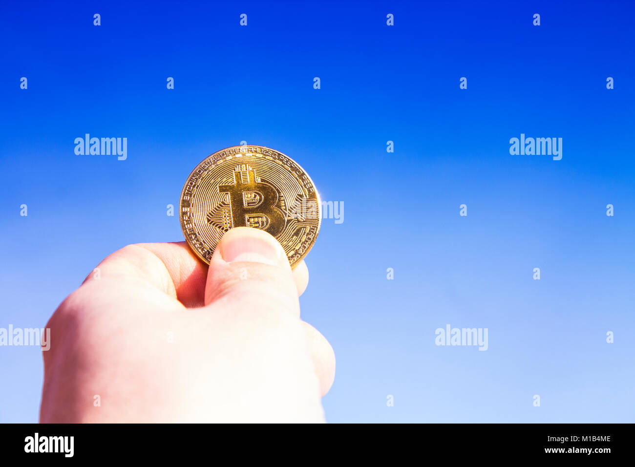 Crypto valuta. Bitcoin. Una mano sollevata detiene una moneta d'oro bit moneta contro il cielo blu. I raggi del sole si riflettono nella stessa moneta. Foto Stock