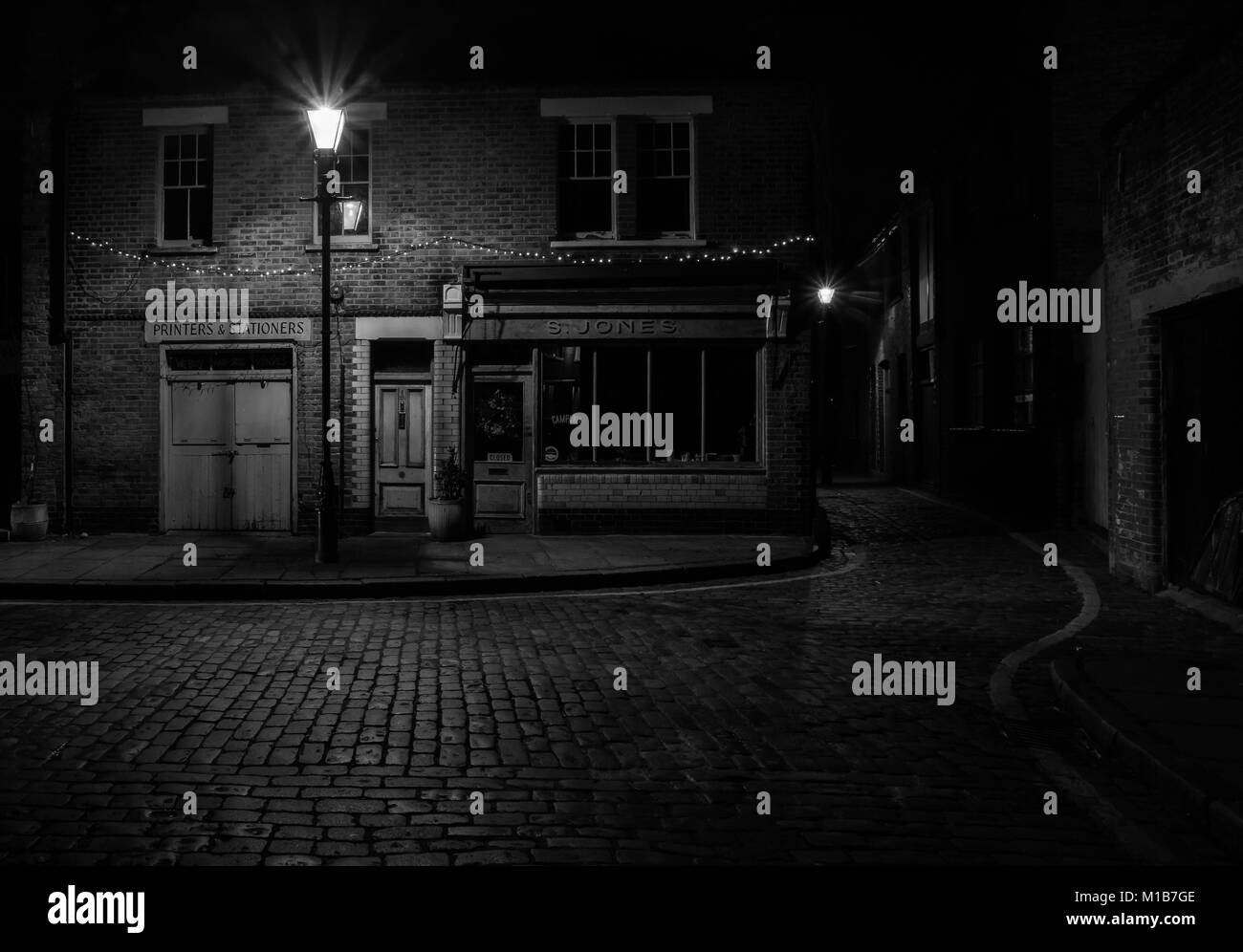S. Jones cafe su Ezra Street, Londra, Regno Unito durante la notte con la strada di ciottoli e il cafe illuminato da una vecchia strada lampada. Foto Stock