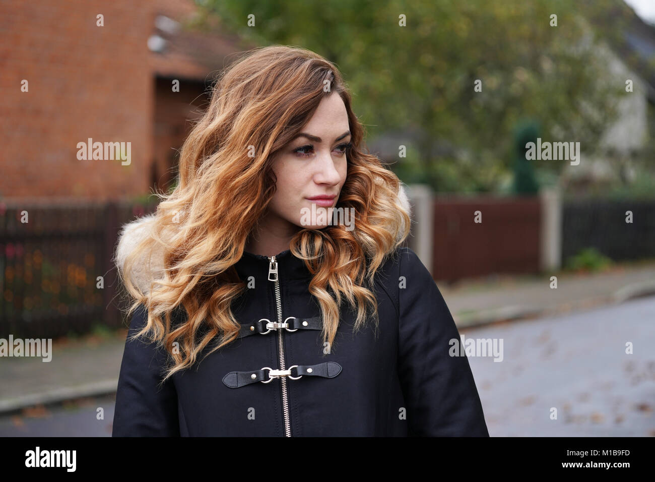 Considerato giovane donna indossa cappotto invernale sulla strada suburbana Foto Stock