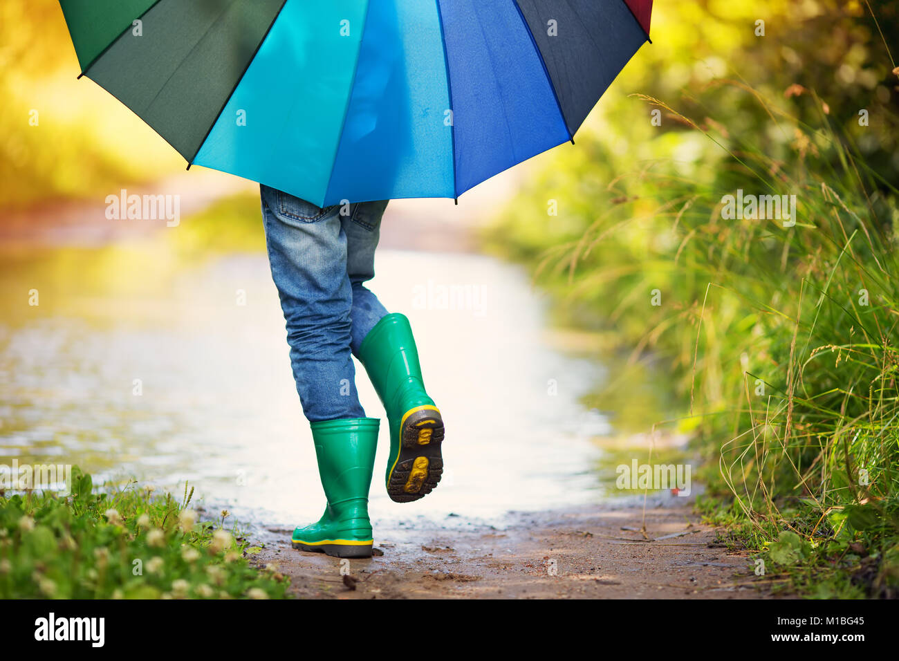 Bambino a piedi nella wellies in una pozza sul tempo piovoso Foto Stock