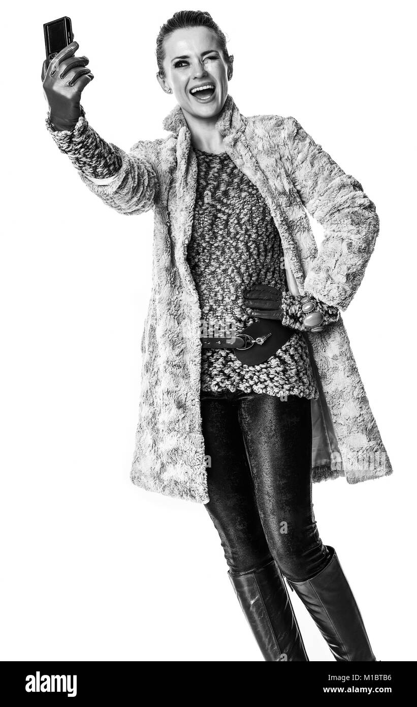 In inverno le cose. Felice donna elegante in inverno coat isolato su bianco con fotocamera digitale prendendo selfie Foto Stock