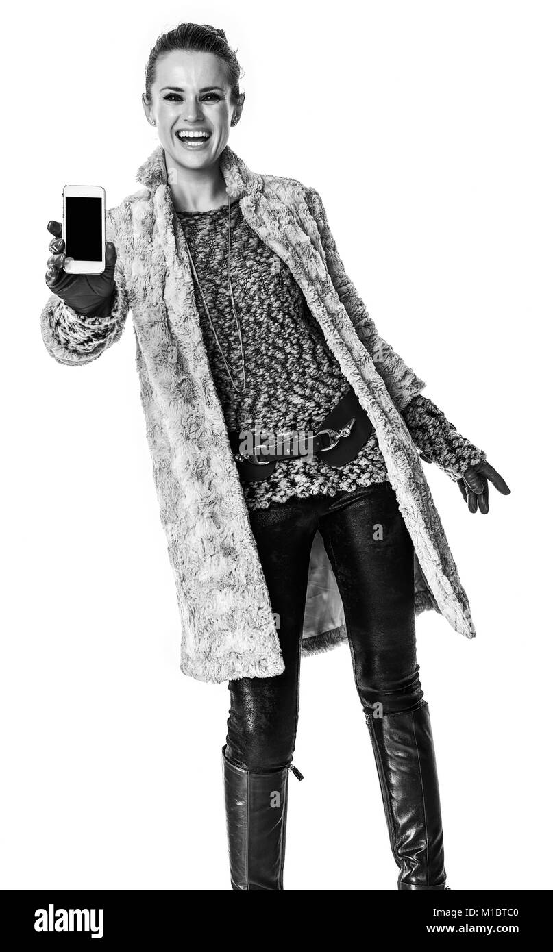 In inverno le cose. sorridente giovane donna in cappotto invernale isolato su bianco che mostra Telefono nella schermata vuota Foto Stock