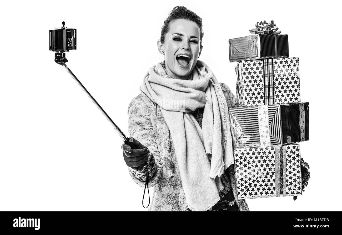 Cose d'inverno. A piena lunghezza Ritratto di sorridente giovane donna in cappotto invernale isolato su bianco con pila di regalo di Natale le caselle tenendo selfie utilizzando s Foto Stock