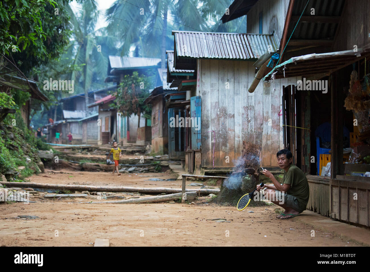 Un uomo sta fumando una sigaretta alla mattina presto in Ban Hat Sa villaggio in fron del suo negozio, Nord del Laos, Asia Foto Stock