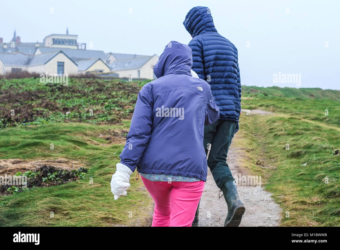 Regno Unito Inverno Meteo - due persone walkers difficoltà a camminare contro vento alta sulla costa di Newquay Cornwall. Foto Stock