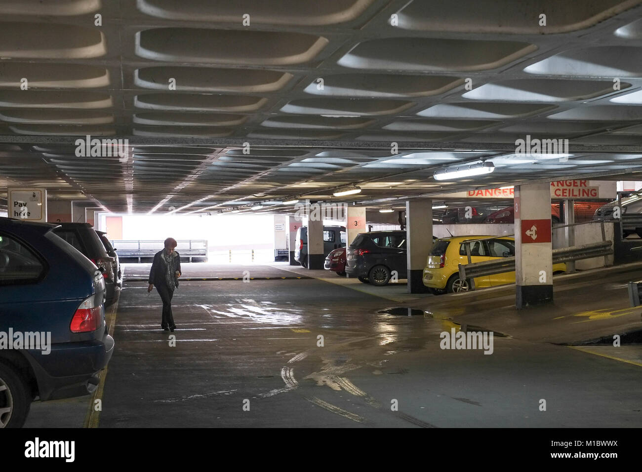 Una donna sola a piedi per la sua auto in un cupo multi-story parcheggio. Foto Stock