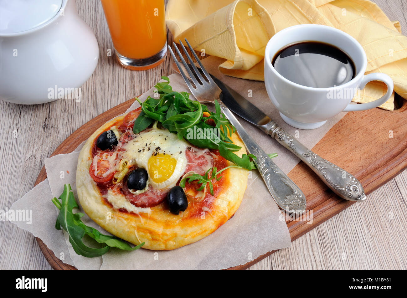 Mini pizza con salsicce e uova e rucola, una tazza di caffè per la prima colazione Foto Stock