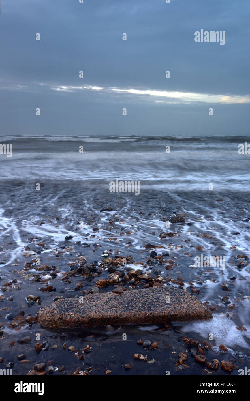 Una grande roccia su una spiaggia in un paesaggio marino con paesaggi e mare mosso su un giorno di tempesta. Impostazione della pressione atmosferica sull'Isola di Wight litorale con moody sky. Foto Stock