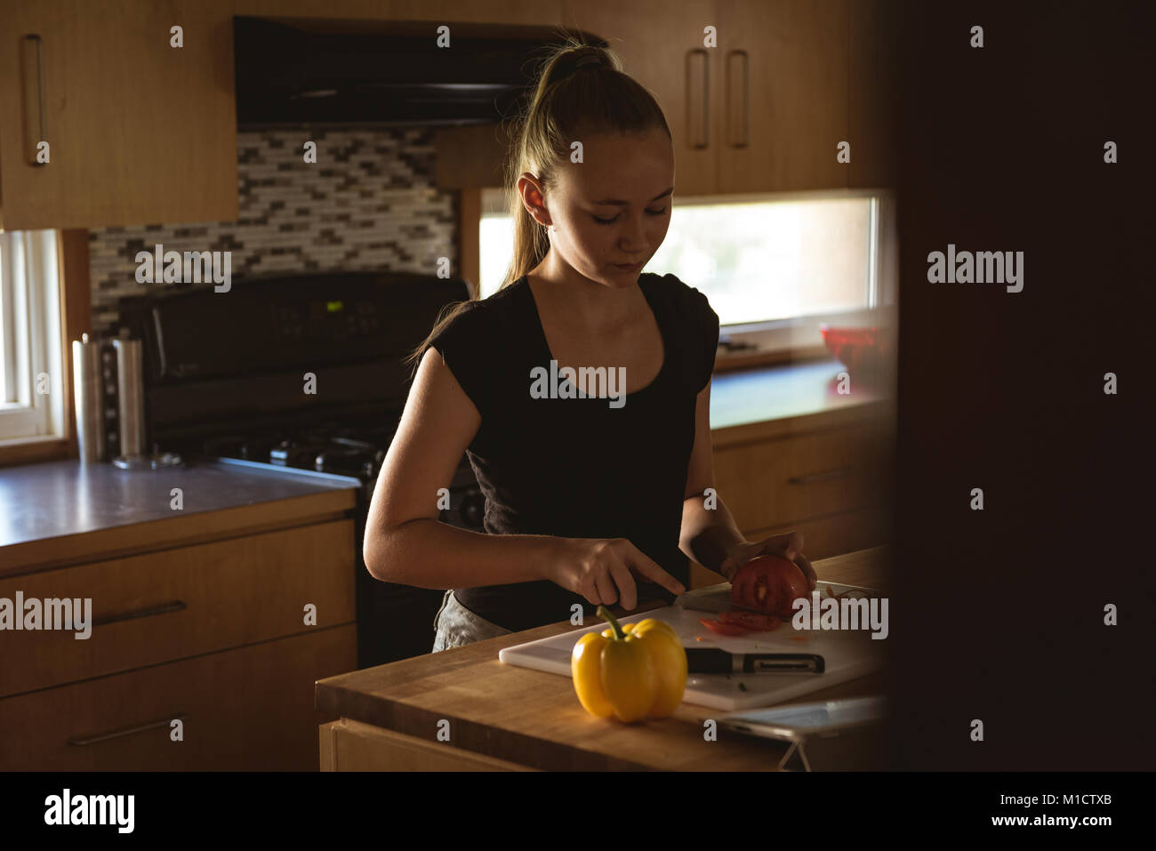 Ragazza in piedi in cucina il pomodoro di taglio con il coltello Foto Stock