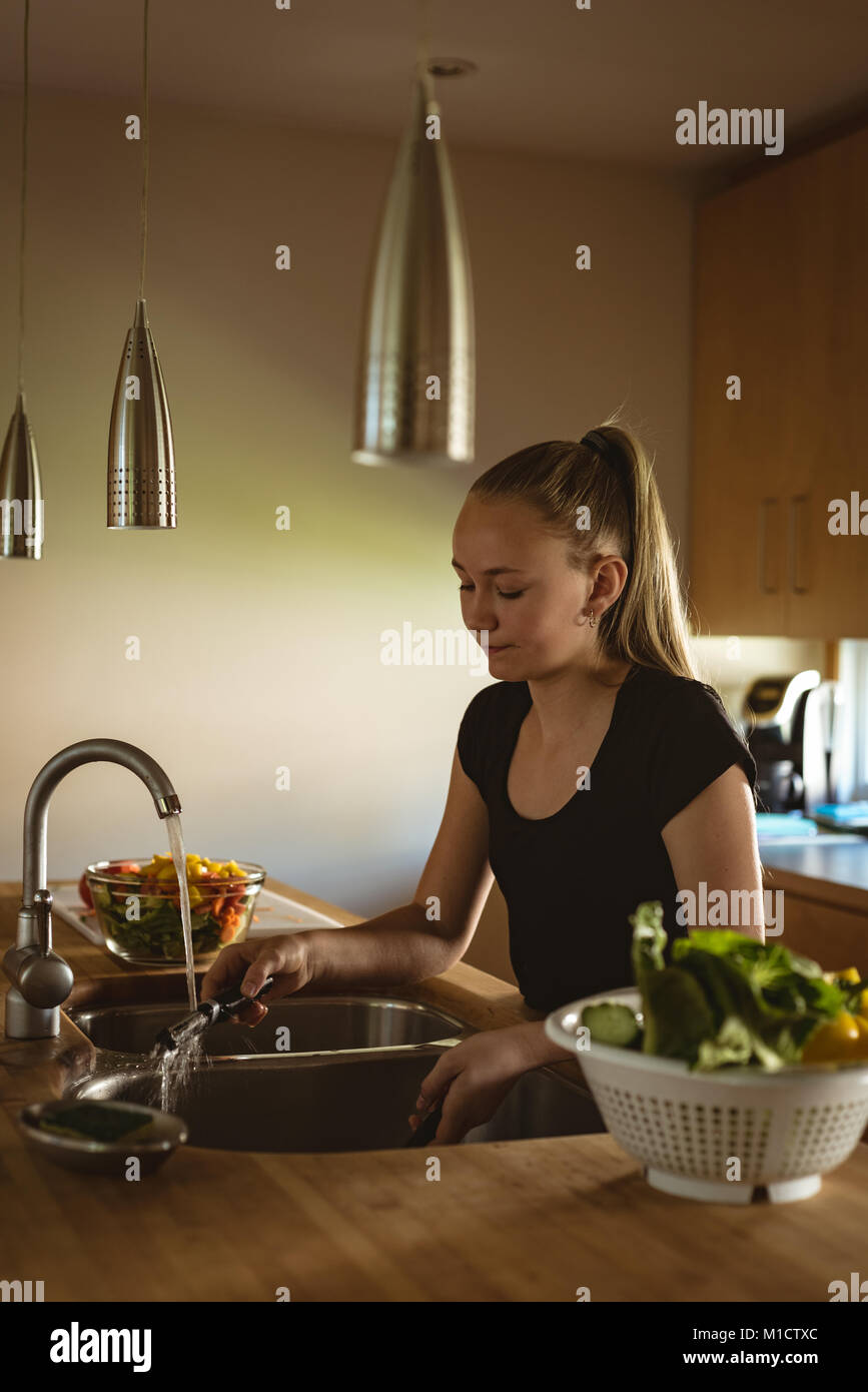 Ragazza in piedi in cucina sbucciatore di lavaggio sotto acqua di rubinetto Foto Stock