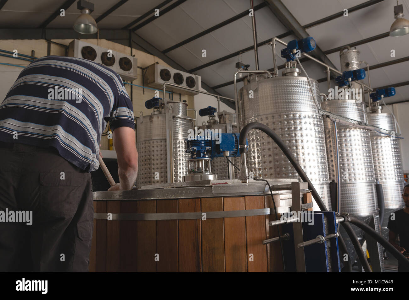 Vista posteriore del lavoratore di sesso maschile agitazione gin in distilleria in fabbrica Foto Stock