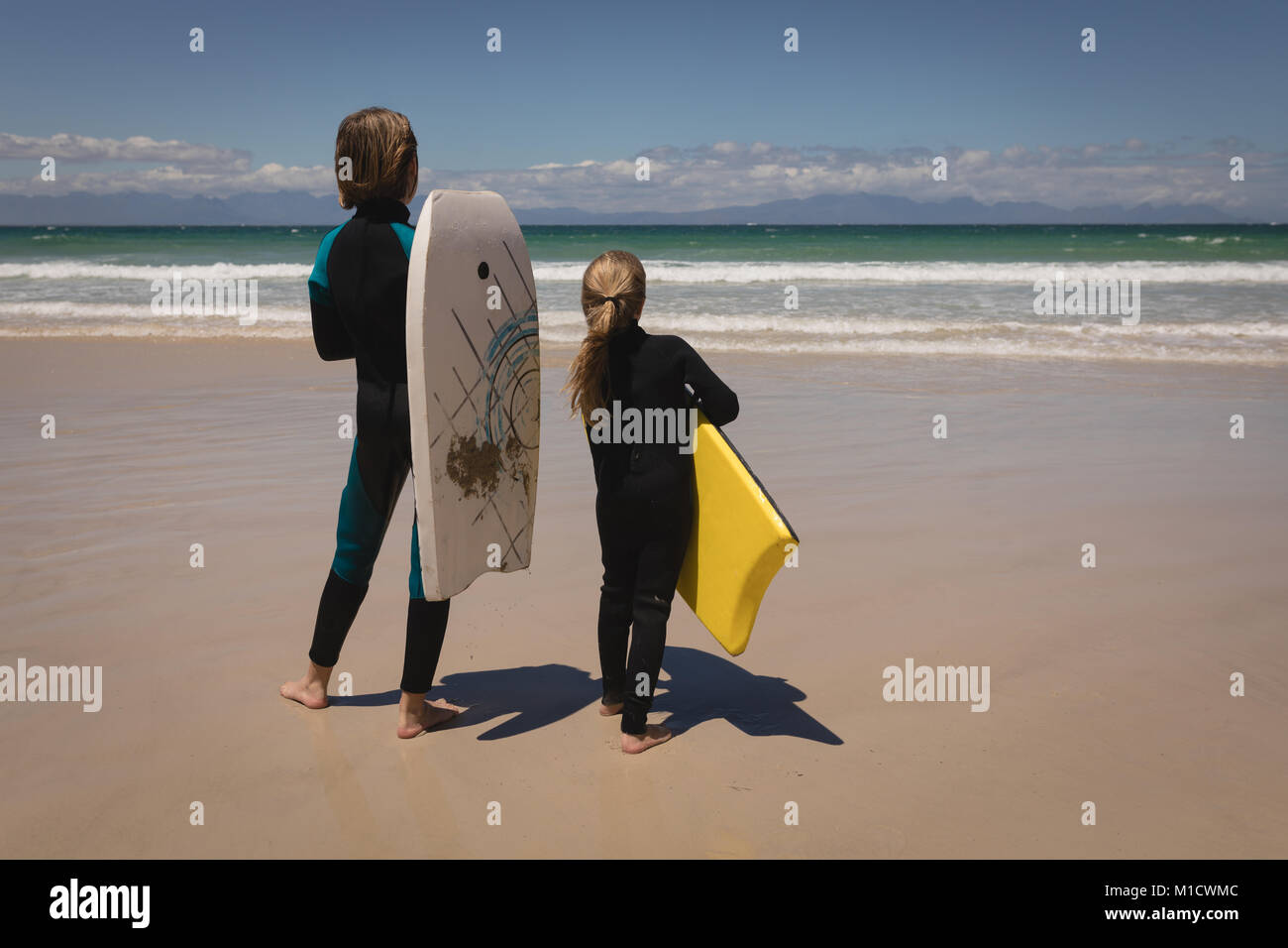 Vista posteriore dei fratelli muta in piedi con la tavola da surf Foto Stock