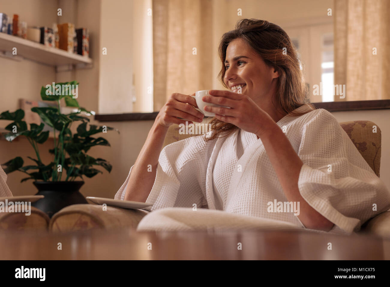 Donna sorridente in accappatoio seduti su una sedia e di bere il caffè a health spa. Femmina presentando un caffè e un momento di relax a spa salone. Foto Stock