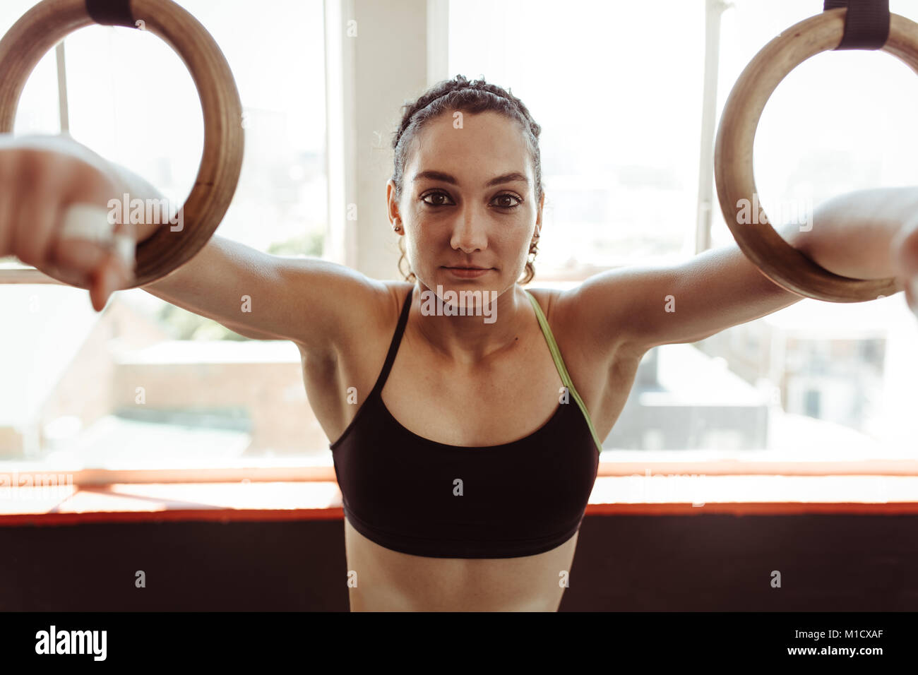 Sano giovane donna esercitando con anelli di ginnastica. Atleta femminile allenamento con anelli di palestra e guardando la fotocamera. Foto Stock