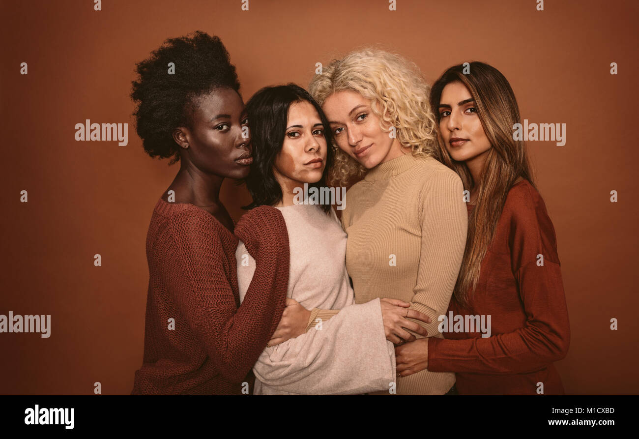 Gruppo di bellissima femmina amici in piedi insieme su sfondo marrone. Multi etnico di donne in studio guardando la fotocamera. Foto Stock