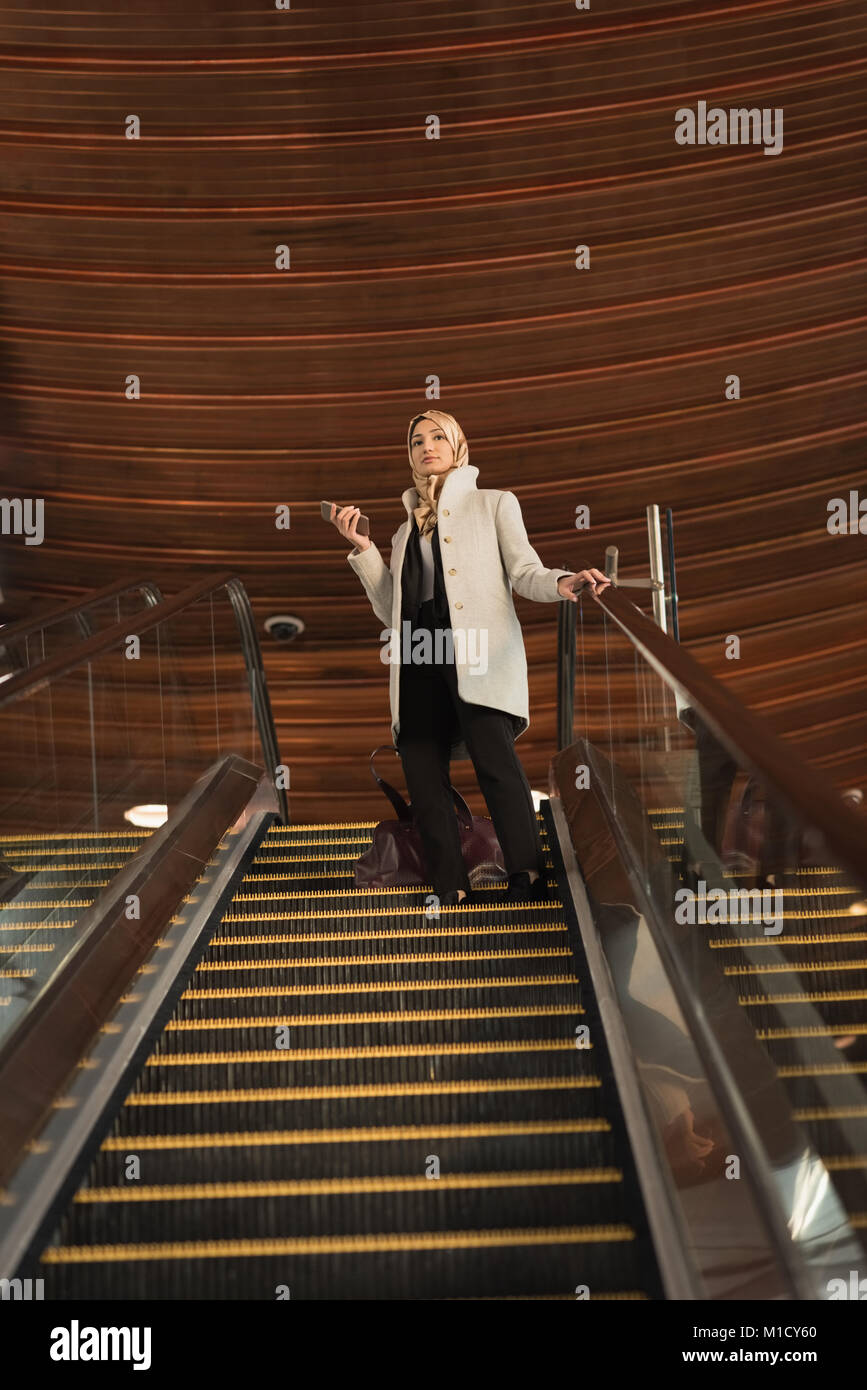 Donna in hijab si sta spostando verso il basso dal escalator Foto Stock