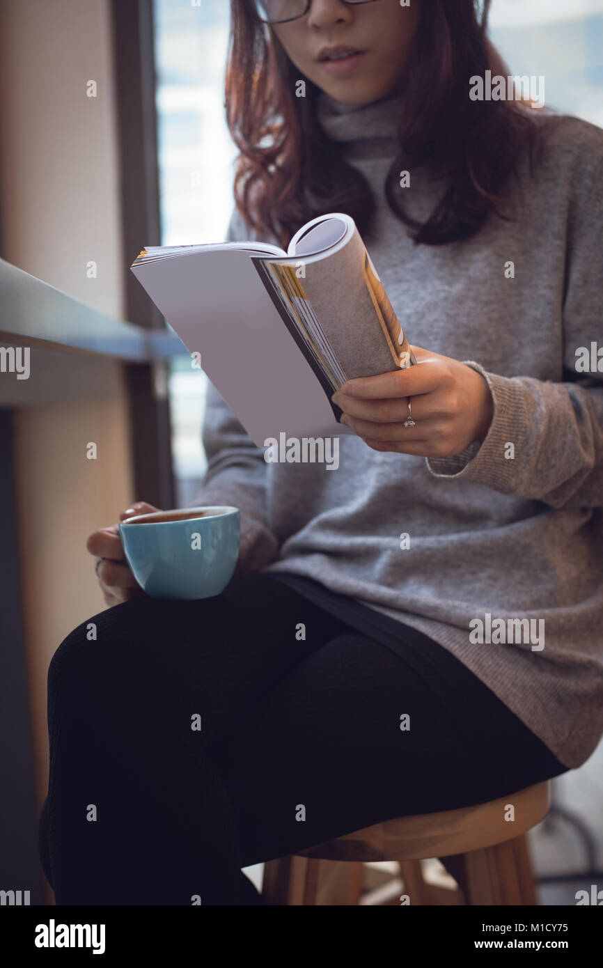 La sezione centrale della donna rivista di lettura mentre un caffè Foto Stock
