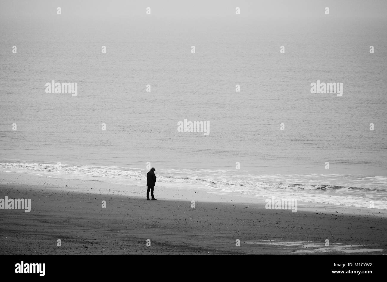 Un uomo solo su una spiaggia di fronte al mare. Foto Stock