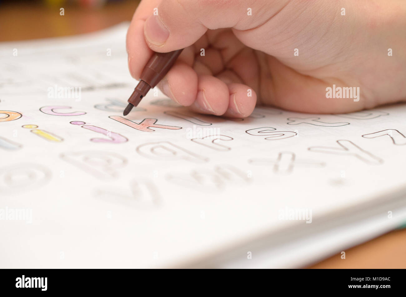 Un bambino scrive a mano e visualizza lettere inglesi in un notebook e di un alfabeto con una matita e pennarello. Foto Stock