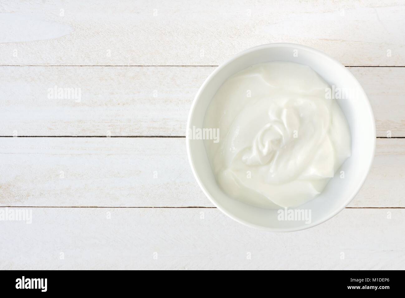 Lo yogurt greco in una ciotola bianca, vista sopra un bianco sullo sfondo di legno Foto Stock