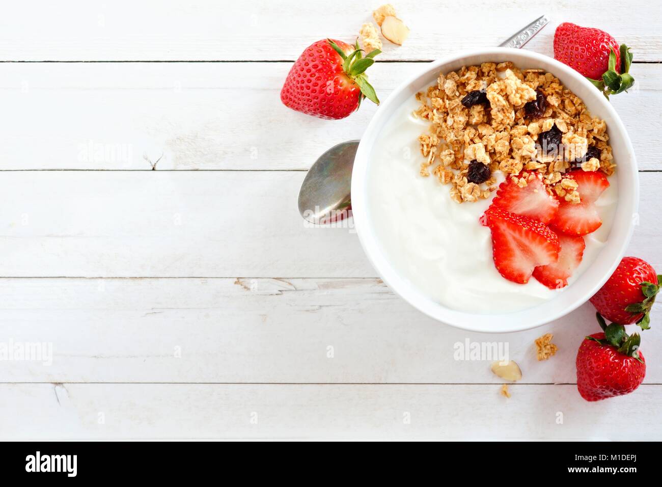Ciotola di yogurt con fragole e muesli, oltre un legno bianco sullo sfondo. Piatto, laici orientamento laterale. Foto Stock