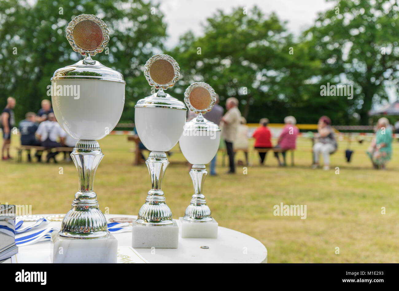 Tre coppe d'argento su una tabella con un campo sportivo in background Foto Stock