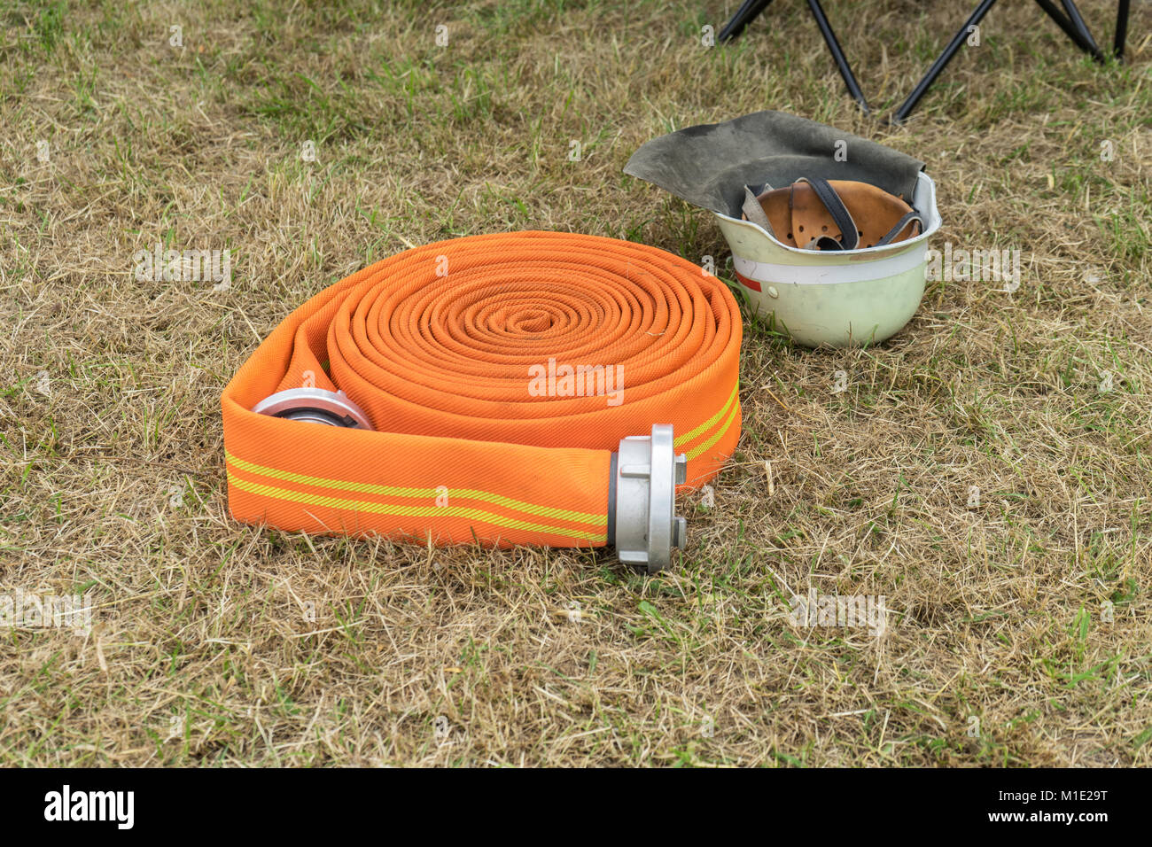 Orange fire il tubo flessibile e il casco di sicurezza si trovano sul prato Foto Stock